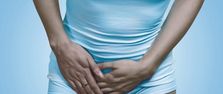 Close up cropped image of a woman with hands holding her crotch lower abdomen isolated on blue background